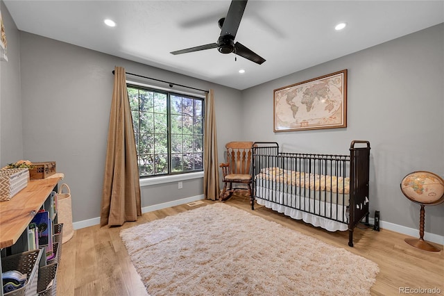 bedroom featuring baseboards, a nursery area, light wood-style flooring, recessed lighting, and a ceiling fan