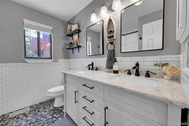 full bathroom featuring a wainscoted wall, tile walls, toilet, and double vanity
