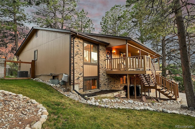 view of side of home with brick siding, central AC, stairway, a lawn, and a wooden deck