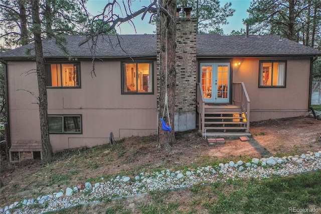 view of front of property featuring french doors, a chimney, and roof with shingles