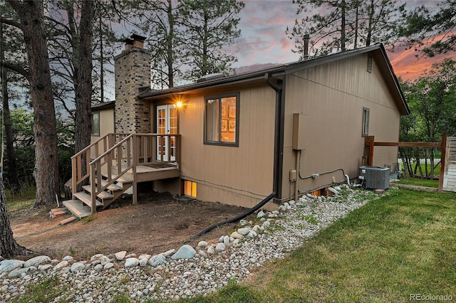 view of side of home with a chimney, cooling unit, and a lawn