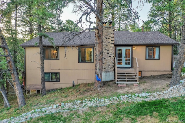 view of front facade with french doors, a shingled roof, and a chimney