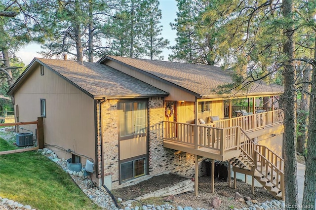back of property featuring a shingled roof, a deck, brick siding, stairs, and cooling unit