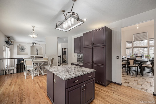 kitchen with decorative light fixtures, dark brown cabinets, a center island, and light hardwood / wood-style flooring