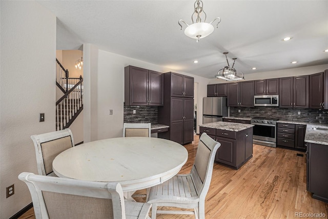 kitchen featuring appliances with stainless steel finishes, a center island, pendant lighting, light wood-type flooring, and dark brown cabinets