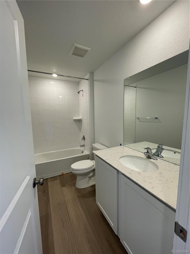 full bathroom with tiled shower / bath combo, vanity, hardwood / wood-style floors, and toilet