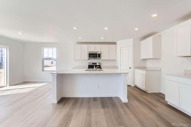 kitchen featuring stainless steel microwave, light wood finished floors, white cabinets, and light countertops