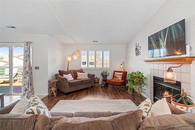 living room with healthy amount of natural light, a tiled fireplace, wood finished floors, and baseboards