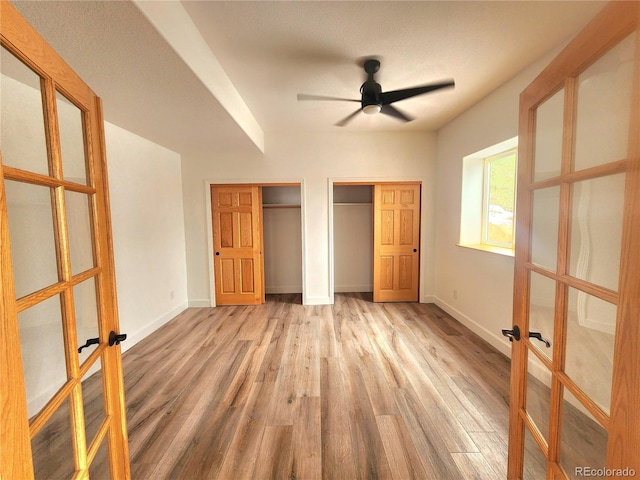 unfurnished bedroom featuring multiple closets, ceiling fan, light wood-type flooring, and french doors