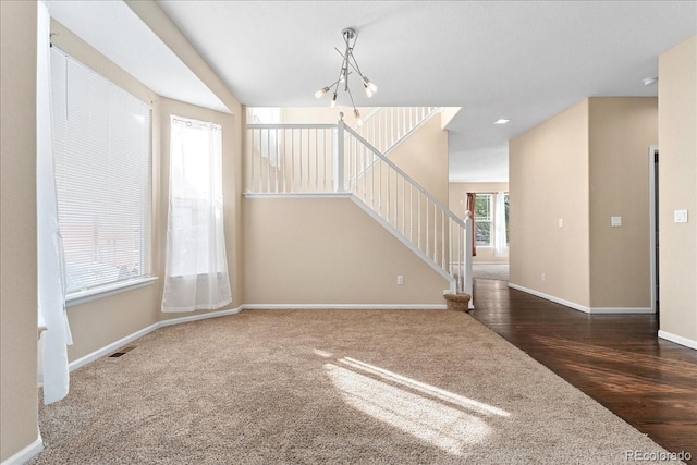 unfurnished living room with visible vents, wood finished floors, an inviting chandelier, baseboards, and stairs