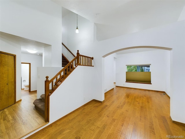 interior space with light wood finished floors, stairs, a high ceiling, and arched walkways