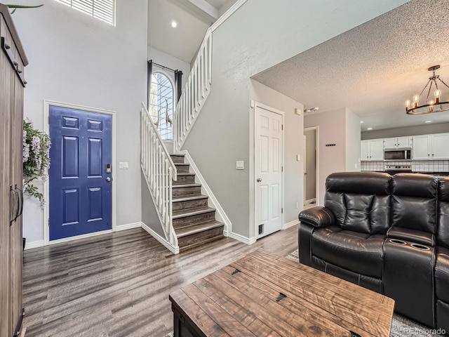 living area featuring stairway, a chandelier, wood finished floors, a high ceiling, and a textured ceiling