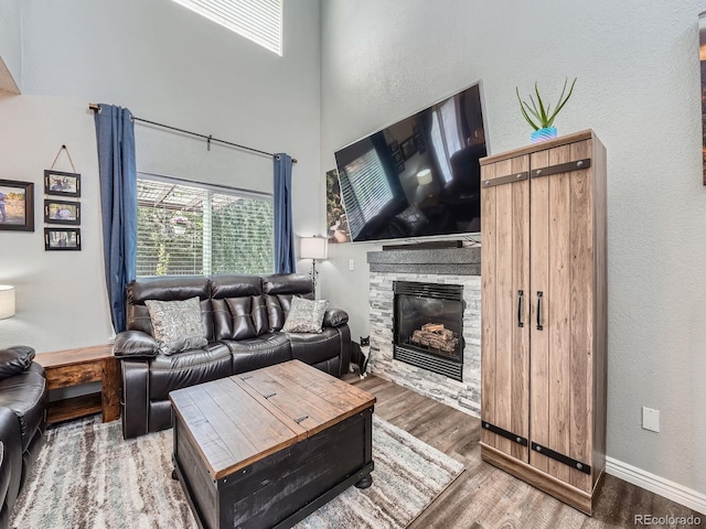 living area with wood finished floors, a fireplace, a textured wall, baseboards, and a high ceiling