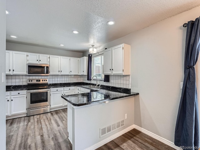 kitchen with appliances with stainless steel finishes, a sink, wood finished floors, white cabinetry, and recessed lighting
