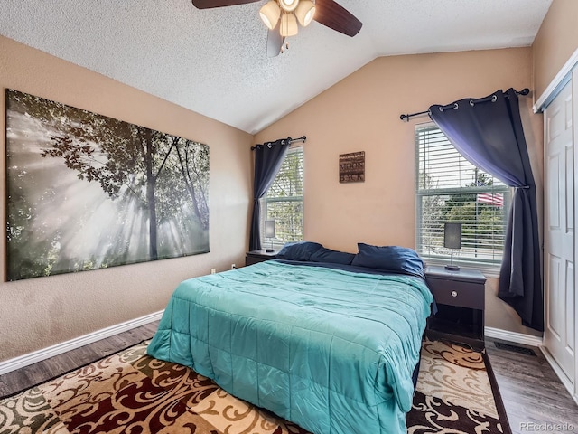 bedroom with wood finished floors, a textured ceiling, vaulted ceiling, baseboards, and ceiling fan