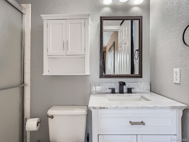 full bath featuring toilet, vanity, a shower with door, and a textured wall