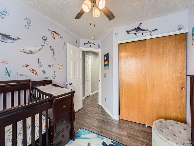 bedroom with a textured ceiling, wood finished floors, a closet, a nursery area, and a ceiling fan