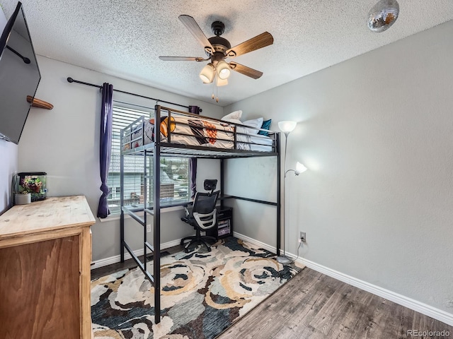 bedroom with an office area, wood finished floors, a textured ceiling, baseboards, and ceiling fan