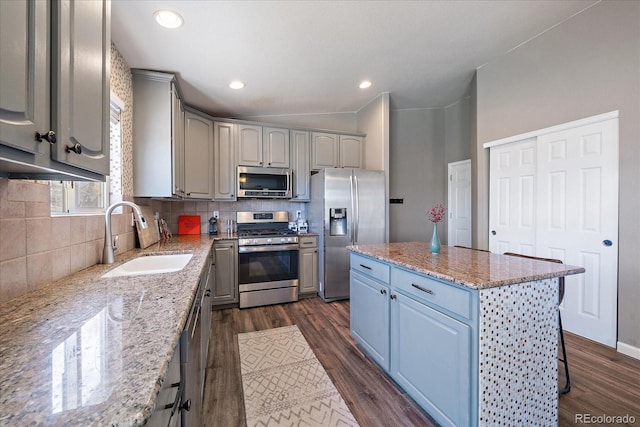 kitchen featuring gray cabinetry, sink, light stone counters, a kitchen island, and appliances with stainless steel finishes