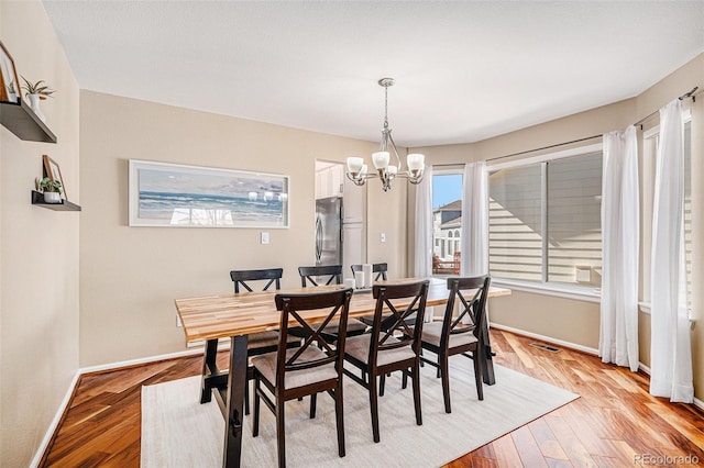 dining space featuring baseboards, visible vents, light wood-style flooring, and an inviting chandelier