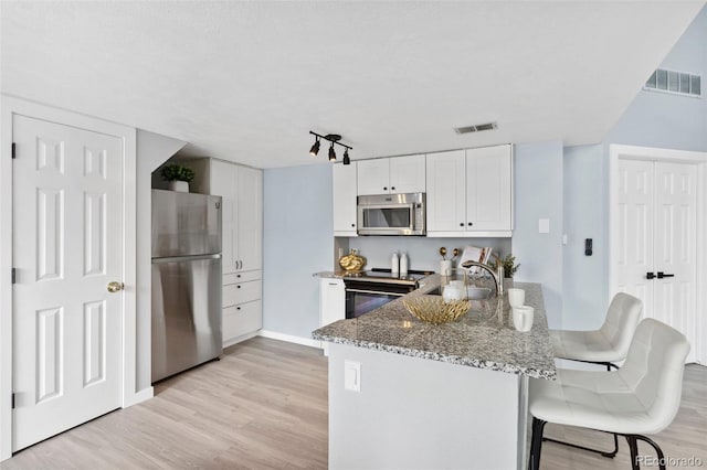 kitchen with stainless steel appliances, a sink, light wood-style floors, stone countertops, and white cabinetry