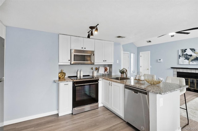 kitchen with stainless steel appliances, a sink, a peninsula, light wood-type flooring, and lofted ceiling