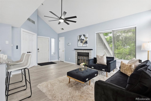 living area featuring high vaulted ceiling, light wood-type flooring, ceiling fan, a fireplace, and baseboards