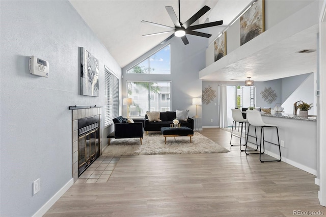 living room with a tiled fireplace, ceiling fan, wood finished floors, baseboards, and a textured wall