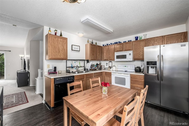 kitchen featuring a textured ceiling, a sink, white appliances, light countertops, and dark wood-style flooring