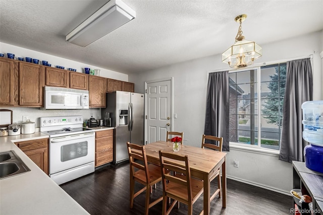 kitchen featuring dark wood finished floors, white appliances, brown cabinets, light countertops, and hanging light fixtures