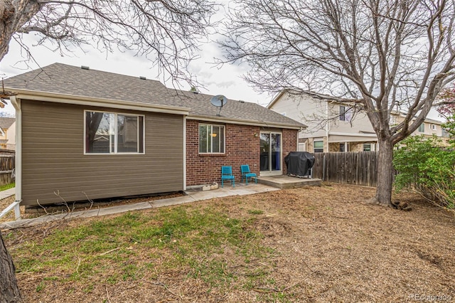 back of house featuring brick siding, a patio area, roof with shingles, and fence