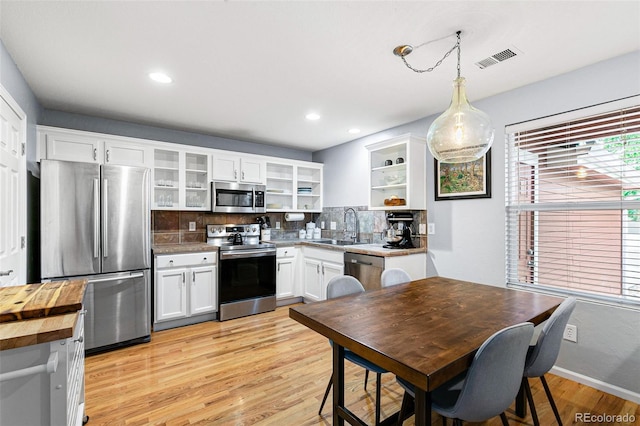 kitchen with pendant lighting, sink, white cabinetry, stainless steel appliances, and light hardwood / wood-style floors