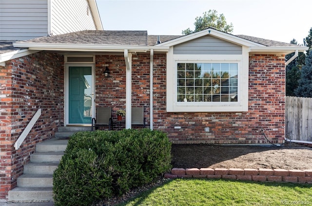 entrance to property featuring roof with shingles, fence, and brick siding