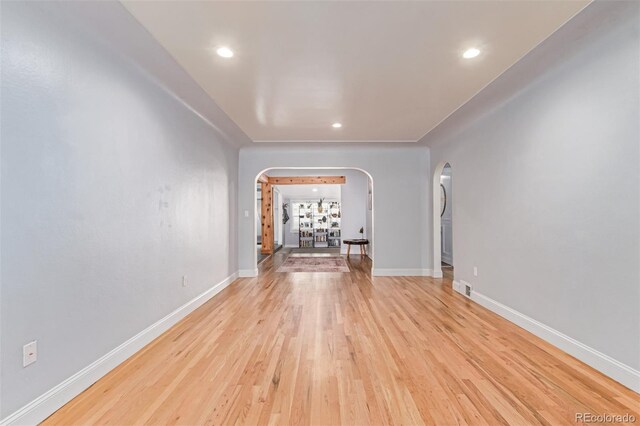 unfurnished room featuring arched walkways, light wood-style flooring, recessed lighting, and baseboards