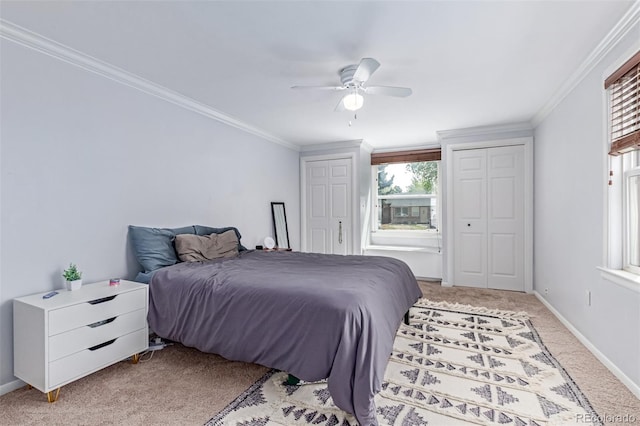 bedroom featuring light colored carpet, two closets, crown molding, baseboards, and ceiling fan