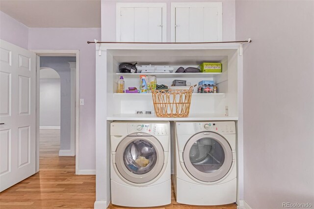 washroom featuring washing machine and clothes dryer, light wood-style flooring, arched walkways, and baseboards