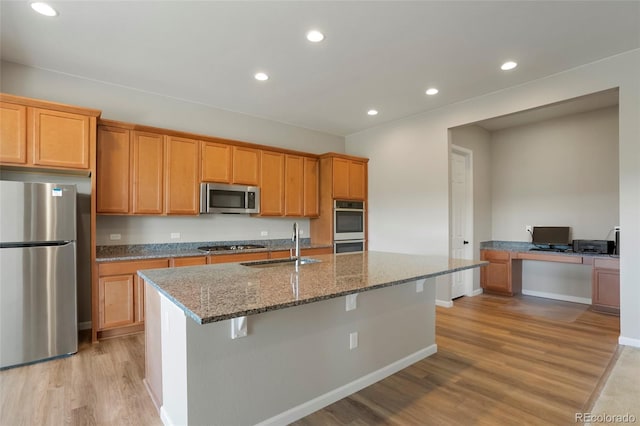 kitchen featuring light wood finished floors, recessed lighting, stone countertops, stainless steel appliances, and a sink