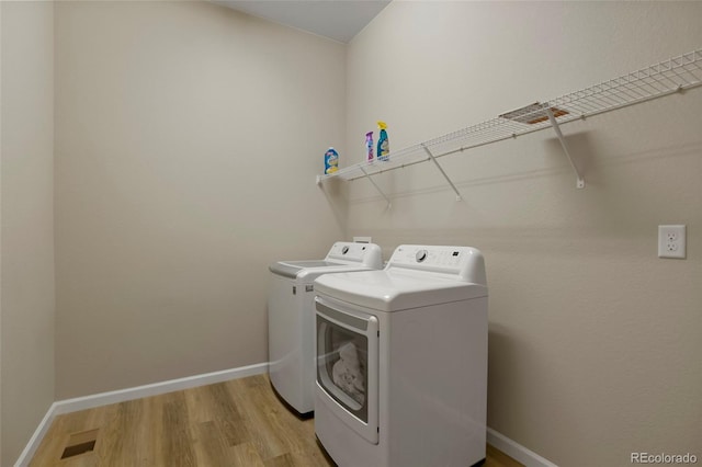 laundry room with light wood-type flooring, baseboards, washing machine and dryer, and laundry area