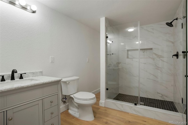 bathroom featuring a marble finish shower, toilet, vanity, and wood finished floors