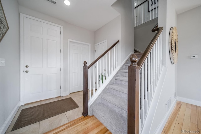 entryway with light wood-style flooring, stairs, baseboards, and visible vents