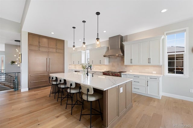 kitchen featuring decorative backsplash, wall chimney exhaust hood, light wood finished floors, and a kitchen breakfast bar