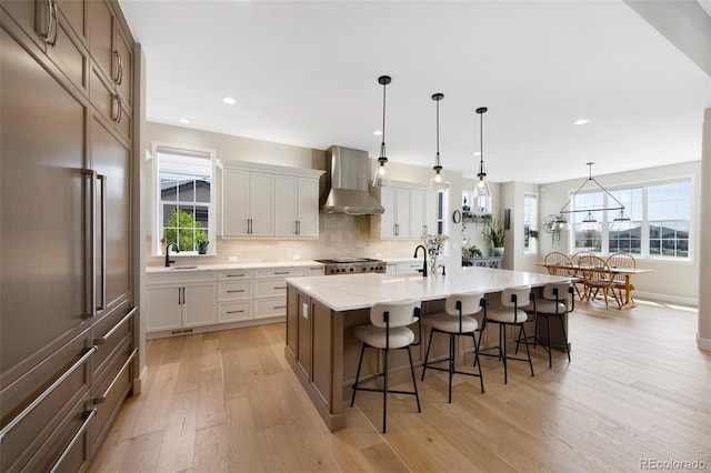kitchen with a breakfast bar, a sink, light wood-style flooring, wall chimney exhaust hood, and decorative backsplash