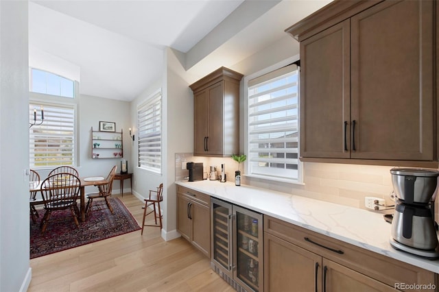 kitchen featuring light wood-style floors, tasteful backsplash, light stone countertops, baseboards, and wine cooler