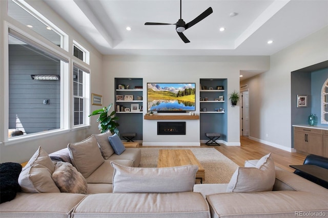 living room featuring recessed lighting, a ceiling fan, light wood finished floors, and a warm lit fireplace