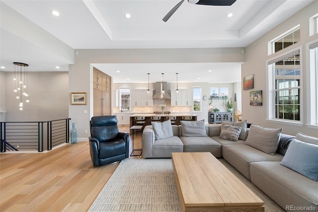 living area featuring ceiling fan, recessed lighting, baseboards, light wood-type flooring, and a tray ceiling