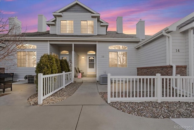 traditional home with a porch, cooling unit, brick siding, and a chimney