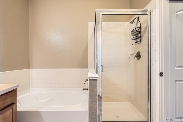 full bath featuring a stall shower, a garden tub, vanity, and a textured wall