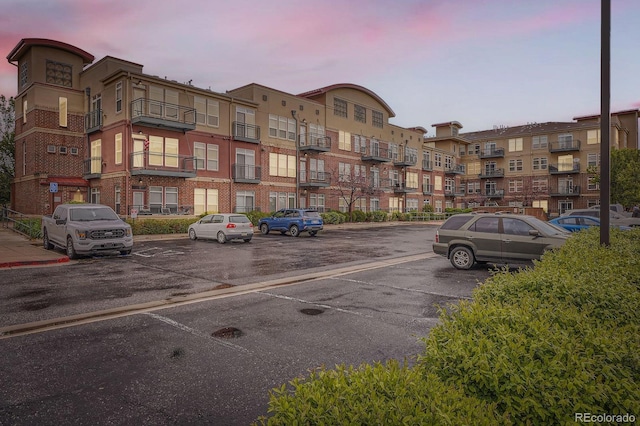 property at dusk with uncovered parking and a view of apartment building / complex