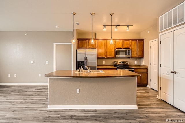 kitchen featuring stainless steel appliances, a sink, brown cabinetry, and wood finished floors