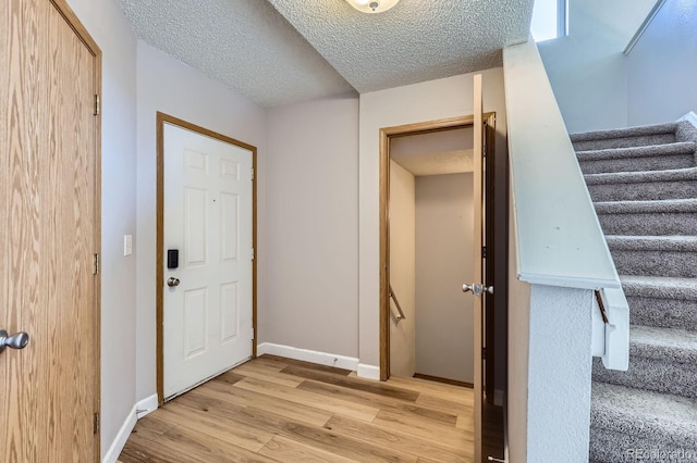 interior space featuring stairway, light wood-style flooring, baseboards, and a textured ceiling